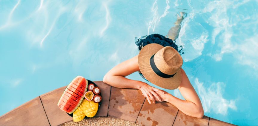 A woman in a pool, with a tray of fruit on the poolside concrete.