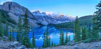 A photo of a lake in front of mountains, surrounded by trees.