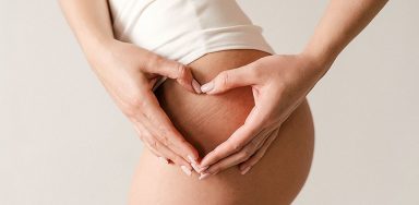 A woman holding her hands in a heart shape over her thigh