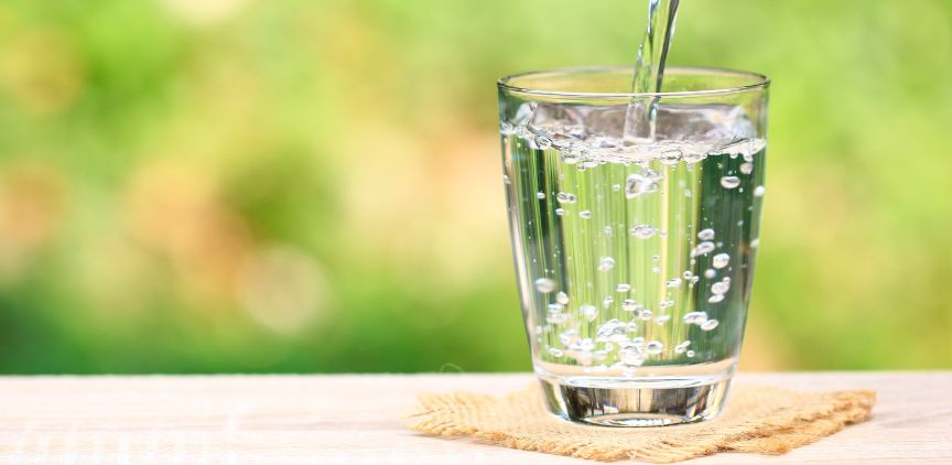 A glass of water sitting on a table, being filled up.