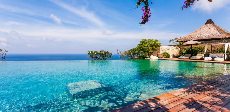 A beach front resort, with clear blue water and lush plants.