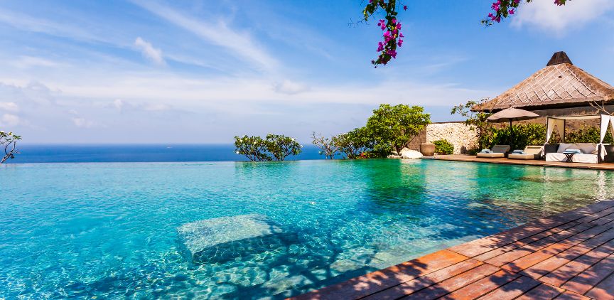 A beach front resort, with clear blue water and lush plants.