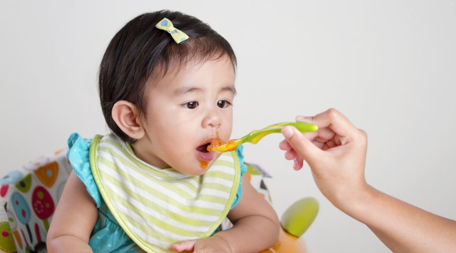 A baby in a highchair being fed with a spoon.