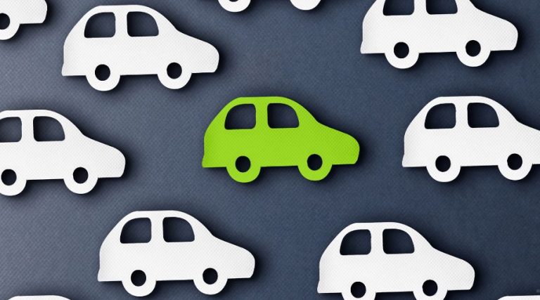 Paper cut outs of white and green cars on a grey background.